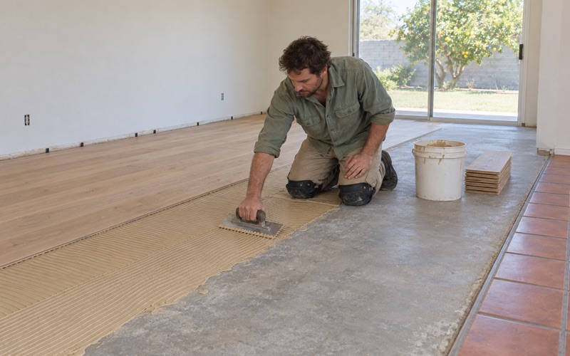 Worker troweling adhesive onto a concrete slab before gluing down engineered oak planks in a Westminster house.